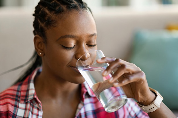 Jonge zwarte vrouw drinkwater thuis kopiëren ruimte