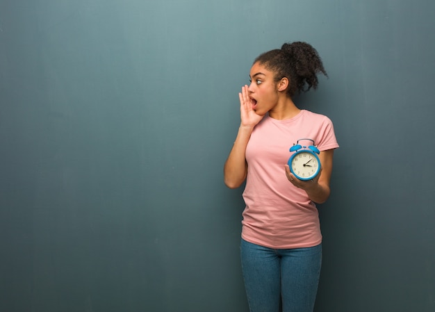 Jonge zwarte vrouw fluistert roddel ondertoon. Ze houdt een wekker vast.