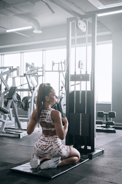 Jonge zwarte vrouw in trainingspak in de sportschool voert oefeningen uit op fitnessapparatuur