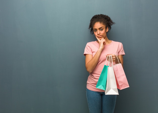 Jonge zwarte vrouw twijfelen en verward. Ze houdt een boodschappentas.