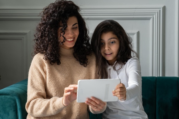 Jonge zwartharige krullende moeder en dochter vieren succes met digitale tablet genieten van zijn