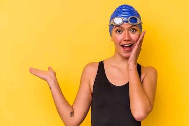 Jonge zwemmer venezolaanse vrouw geïsoleerd op gele achtergrond houdt kopieerruimte op een handpalm, hand over wang. verbaasd en verheugd.