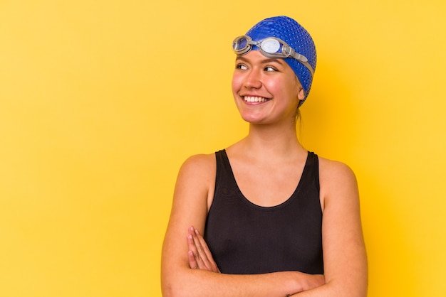 Jonge zwemmer venezolaanse vrouw geïsoleerd op gele muur glimlachend zelfverzekerd met gekruiste armen.