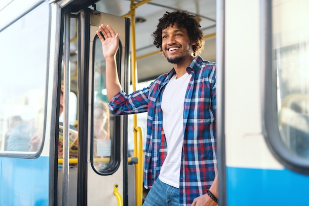 Jongelui die Afrikaanse kerel glimlachen die bij meisje golven terwijl status op de busdeur.