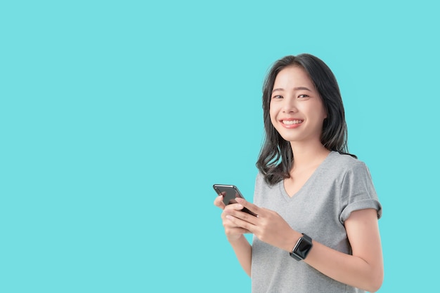 Jongelui die Aziatische smartphone van de vrouwenholding glimlachen en slijtage smartwatch geïsoleerd op lichtblauwe achtergrond.