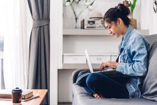 Jongelui die gelukkige mooie Aziatische vrouw ontspannen die thuis gebruikend laptop computer het werken en videoconferentievergadering werken Jong creatief typen op toetsenbordwerk vanuit huis concept