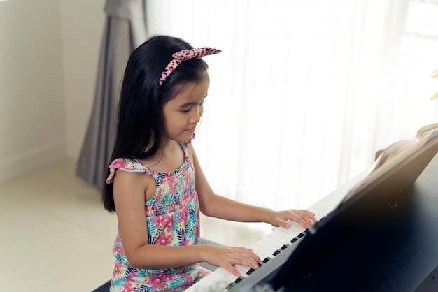 Jongelui weinig aziatisch leuk meisje die elektronische piano thuis spelen.