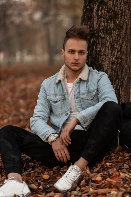 jongeman model in een stijlvol denim blauw jasje poseren in het park