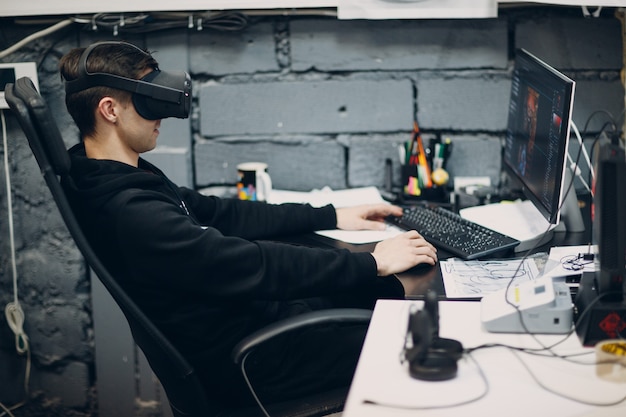Jongeman programmeur gamer zittend op een stoel met computerbureaublad in de buurt van virtual reality bril, vr-bril headset.