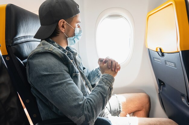 Jongeman reiziger die een preventiemasker draagt tijdens een vlucht in een vliegtuig