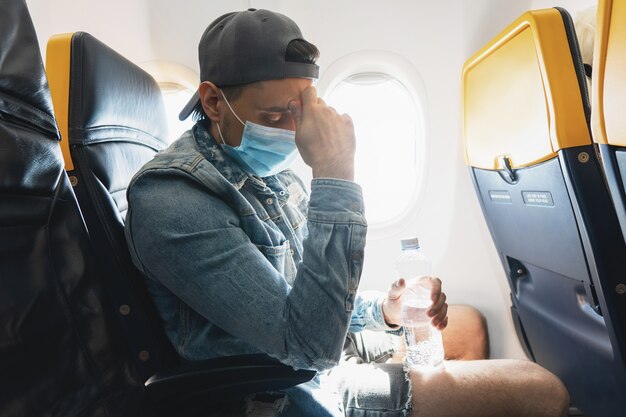 Jongeman reiziger die een preventiemasker draagt tijdens een vlucht in een vliegtuig