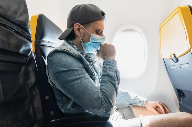 Jongeman reiziger die een preventiemasker draagt tijdens een vlucht in een vliegtuig