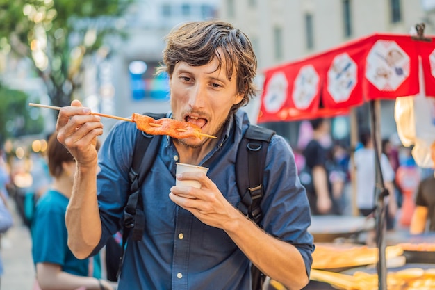 Jongeman toerist die typisch koreaans straatvoedsel eet op een wandelstraat van gekruid fastfood in seoul