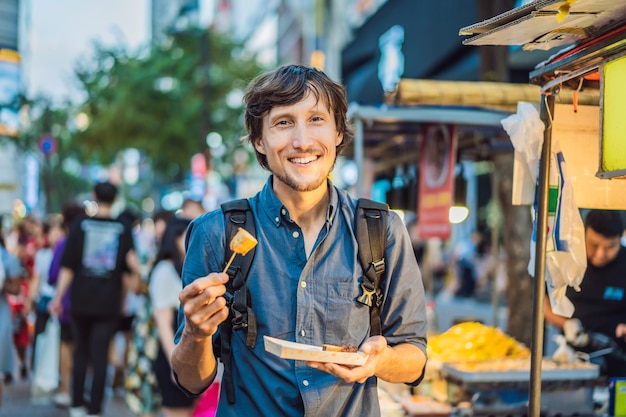 Jongeman toerist die typisch koreaans straatvoedsel eet op een wandelstraat van gekruid fastfood in seoul