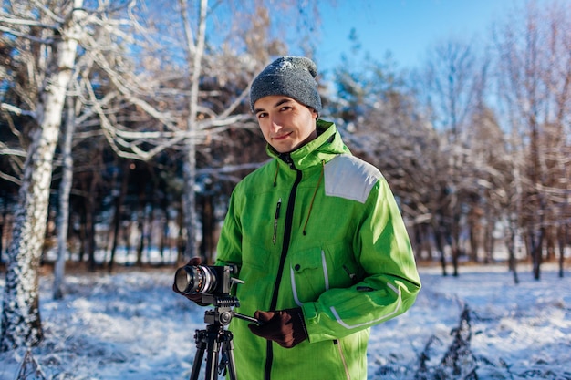 Jongemanfotograaf maakt foto's van besneeuwd winterbos met camera en statief outdoor seizoensgebonden hobbyactiviteiten