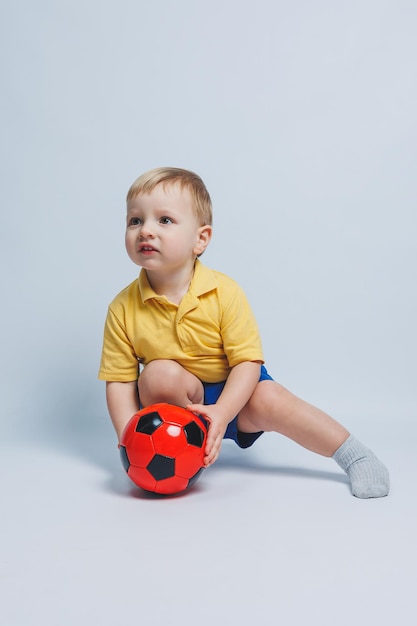 Jongen 34 jaar oude voetbalfan in een gele tshirt met een bal in zijn handen met een voetbal in zijn handen geïsoleerd op een witte achtergrond Het concept van sport familie recreatie