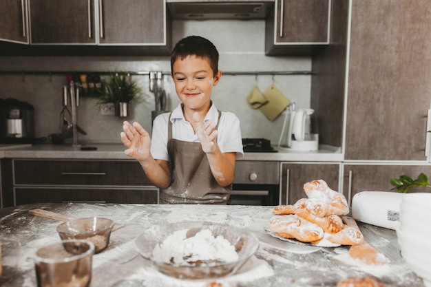 Jongen 8 jaar oud in de keuken speelt met bloem. kind in de keuken bereidt deeg.