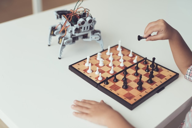 Jongen aan het schaken met een kleine robot aan tafel.