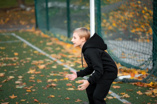 Jongen - atleet staat in de herfst bij de poort op het voetbalveld.