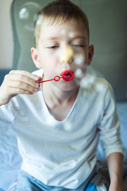 Jongen blaast zeepbellen zittend op de bank thuis veel zeepbellen Interessante spelletjes thuis magische bubbels