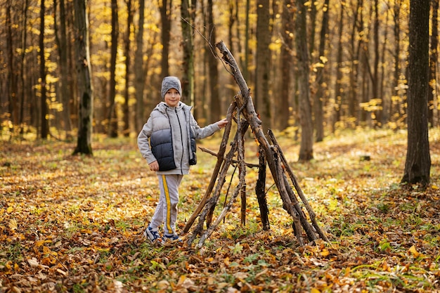 Jongen bouwt een huis van stokken in herfstbos