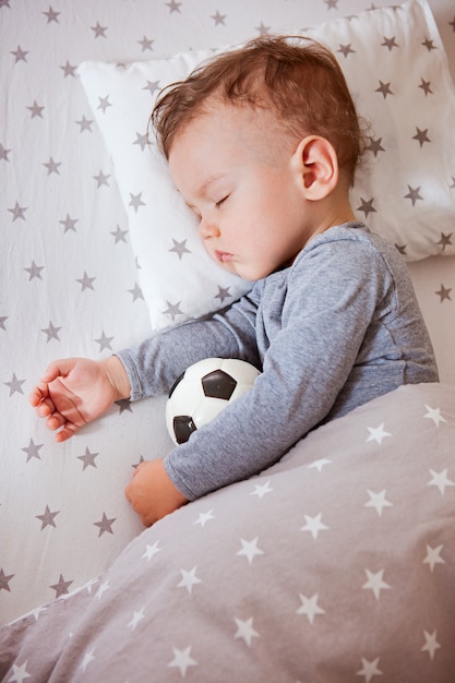 Jongen, de jongen slaapt in een babywieg die een voetbal omhelst