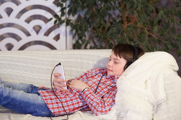 Jongen die aan muziek in hoofdtelefoons met in hand telefoon luistert.