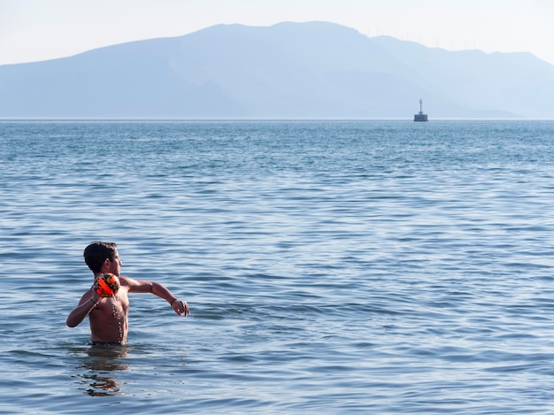 Jongen die bal speelt op het strand in de Egeïsche zee op een Grieks eiland op een zomerdag in Griekenland