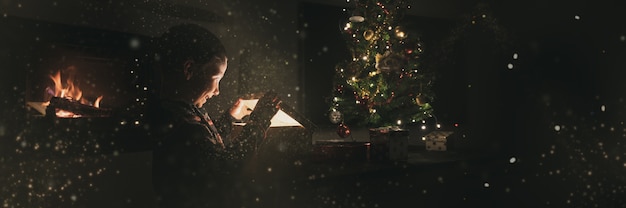 Jongen die een doos van de vakantiegift onder de kerstboom opent met glitters en sprookjesstof