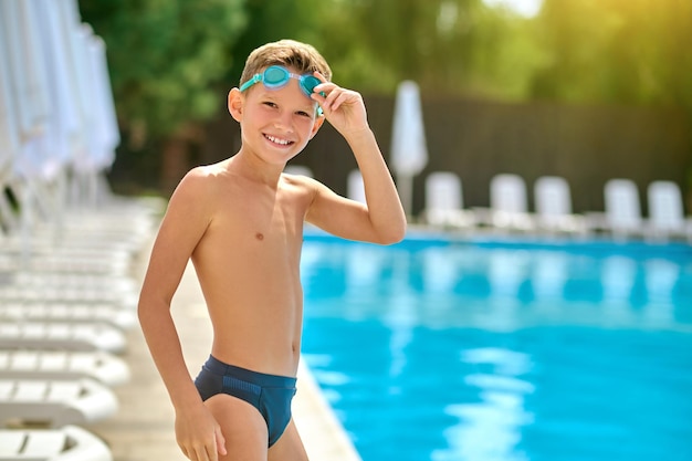 Jongen die een veiligheidsbril aanraakt die naar de camera bij het zwembad glimlacht