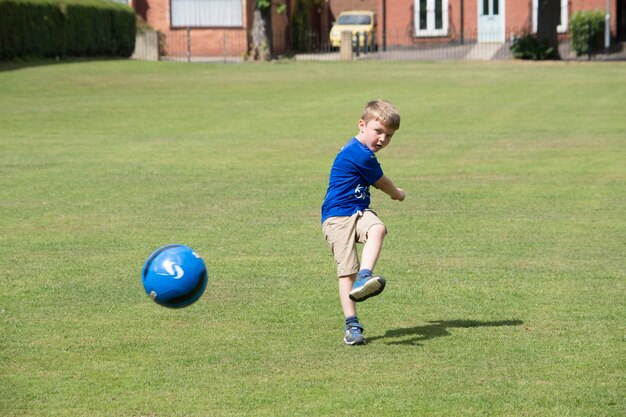 Foto jongen die een voetbal schopt op een grasveld