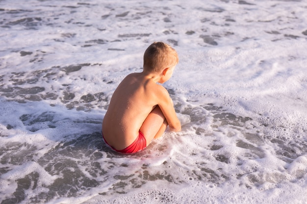 Jongen die in overzeese golven springt. Spring begeleid door waterspatten. Zonnige zomerdag, oceaan kust