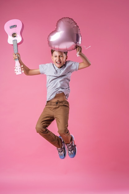 Jongen die met roze ballon en ukelele springt