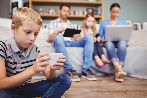 Jongen die mobiele telefoon met behulp van terwijl familie met technologieën