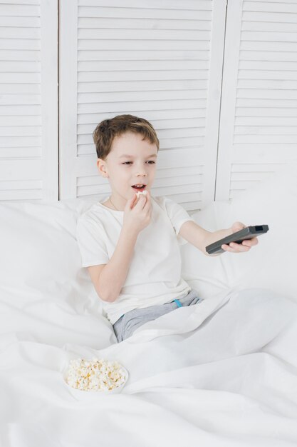 Jongen die popcornzitting in bed eet en op tv let