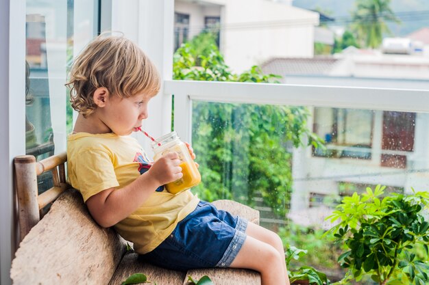 Jongen die sappige smoothie van mango in glazen metselaarkruik drinkt met gestreept rood stro