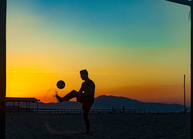 Jongen die sporten met bal op het strand doet in de volle zomerzonsondergang aan de Braziliaanse kust