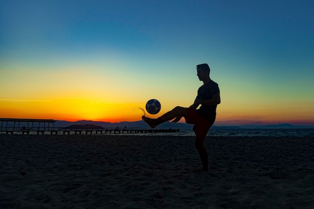 Jongen die sporten met bal op het strand doet in de volle zomerzonsondergang aan de Braziliaanse kust