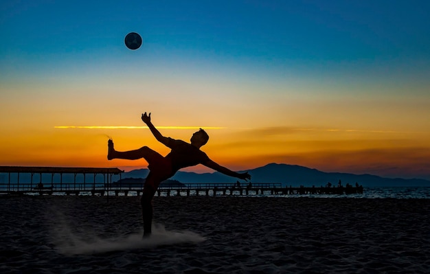 Jongen die sporten met bal op het strand doet in de volle zomerzonsondergang aan de Braziliaanse kust