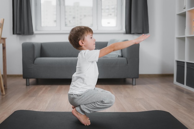 Jongen doet klassieke squats thuis op de vloer op een sportmat