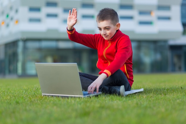 jongen een student van school zittend op het gazon gebruikt een laptop