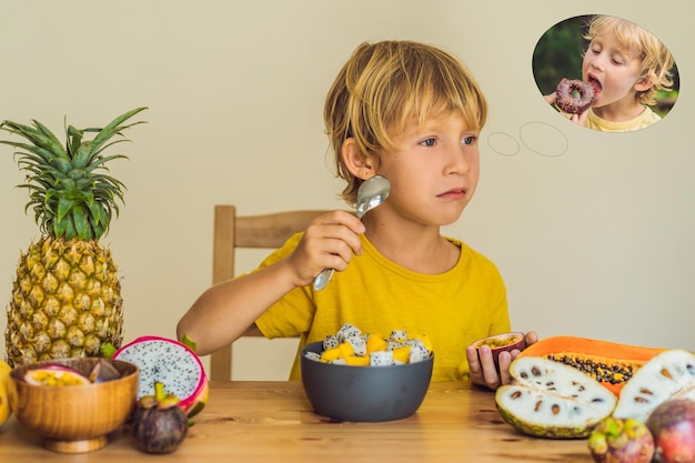 Jongen eet fruit maar droomt over donuts Schadelijk en gezond voedsel voor kinderen Kind eet gezonde snack Vegetarische voeding voor kinderen Vitaminen voor kinderen Junkfood concept