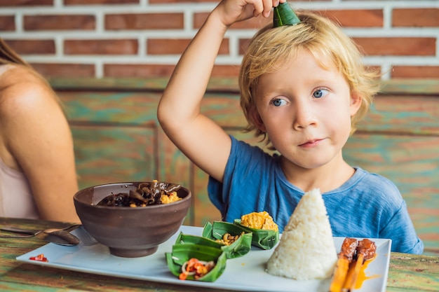 Jongen eet in een café. Levensstijl. Een gerecht bestaande uit rijst, gebakken vis met bospaddenstoelen en verschillende soorten sauzen.