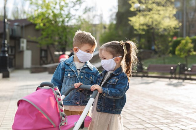 Jongen en een meisje lopen met een kinderwagen in beschermende gezichtsmaskers Concept familie Coronavirus covid19