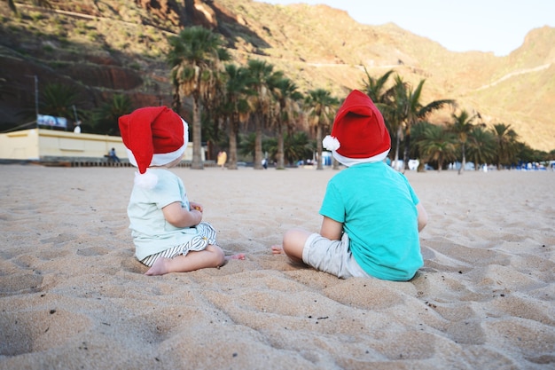 Jongen en meisje in rode kerstmutsen die plezier hebben op het oceaanzandstrand Kinderen spelen op de achtergrond van de zeekust