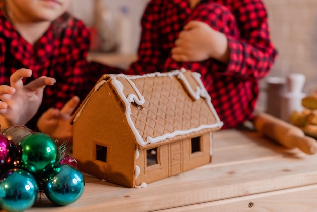 jongen en meisje in rode kerstpyjama bereiden een peperkoekhuis en decoreren het thuis met glazuur