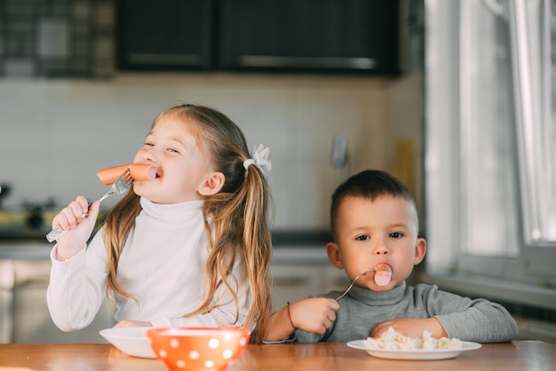 Jongen en meisje kinderen in de keuken worstjes met pasta eten is erg leuk en vriendelijk