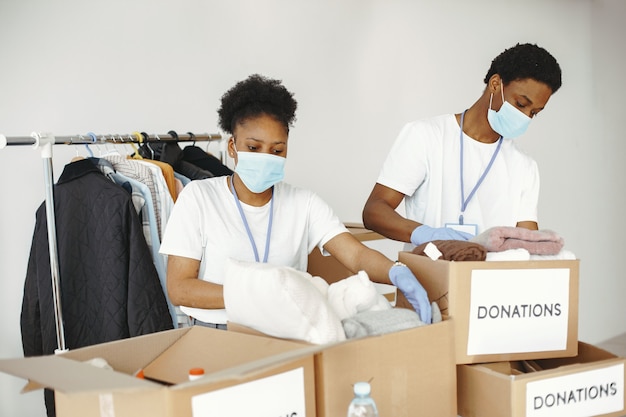 Jongen en meisje met selectievakjes. Afrikaanse vrijwilligers in maskers. Dozen met humanitaire hulp.