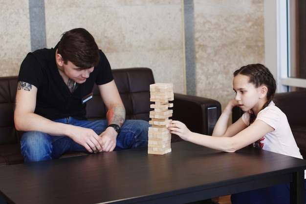 Jongen en meisje tiener bouwen een toren van houten blokken game jenga op de tafel zittend op de bank