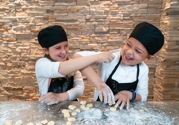 Foto jongen en meisje tweelingbroers en zussen spelen tijdens het koken met meel in koksoutfits